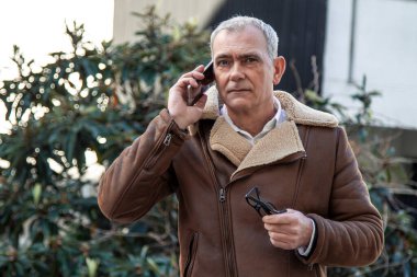 Sokakta cep telefonu kullanan ceketli olgun bir adam.