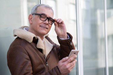 Sokakta cep telefonu kullanan ceketli olgun bir adam.