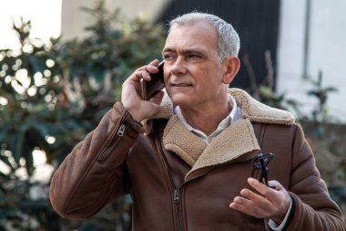 Sokakta cep telefonu kullanan ceketli olgun bir adam.