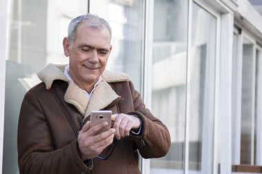 Sokakta cep telefonu kullanan ceketli olgun bir adam.