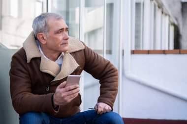 Sokakta cep telefonu kullanan ceketli olgun bir adam.