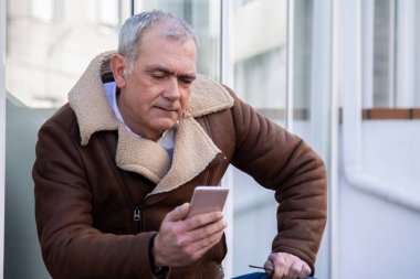 Sokakta cep telefonu kullanan ceketli olgun bir adam.