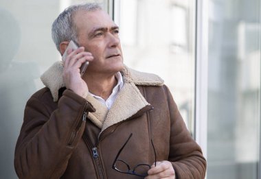 Sokakta cep telefonu kullanan ceketli olgun bir adam.