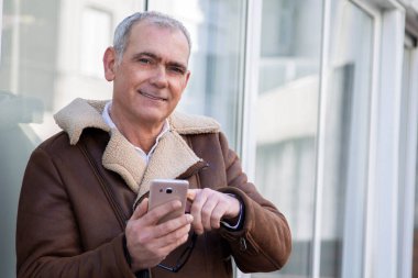 Sokakta cep telefonu kullanan ceketli olgun bir adam.