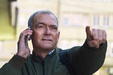 Elinde cep telefonu olan yetişkin bir adam caddede yürüyen bir adresi işaret ediyor.