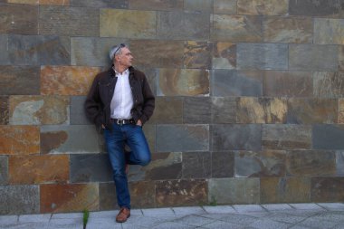 Duvarda kot pantolon ve ceket giyen yetişkin bir adam.