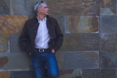 Duvarda kot pantolon ve ceket giyen yetişkin bir adam.