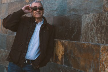 Duvarda kot pantolon ve ceket giyen yetişkin bir adam.