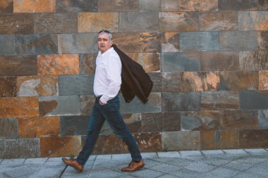 Duvarda kot pantolon ve ceket giyen yetişkin bir adam.