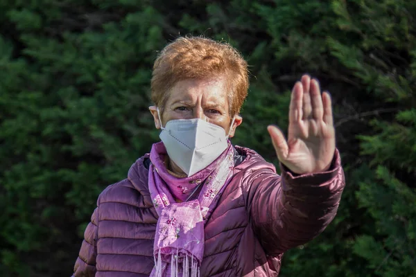 Tıbbi maske takan ve elleriyle dur işareti yapan yaşlı kadın, Coronavirus inkar kavramı.