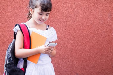 Sırt çantası ve defteri olan öğrenci kız cep telefonu kullanıyor.