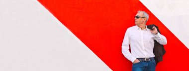 Duvara yaslanmış güneş gözlüklü zarif olgun bir adam.