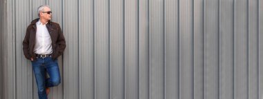 Duvara yaslanmış güneş gözlüklü zarif olgun bir adam.