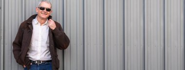 Şehir körüne yaslanan güneş gözlüklü zarif olgun bir adamın portresi.