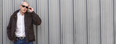 Şehir körüne yaslanan güneş gözlüklü zarif olgun bir adamın portresi.