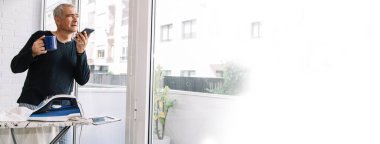 Adam evde gömlek ütülerken cep telefonu kullanıyor, boşluğu kopyala