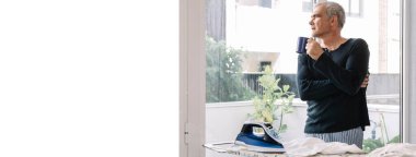 Evdeki gömleği ütülerken kahve içen bir adam.