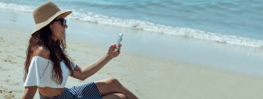 Plajdaki kadın cep telefonunu kopyalamak için kullanıyor.