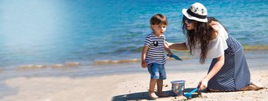 Anne ve oğlu sahilde fotokopi aletiyle kova ve kürekle oynuyor.