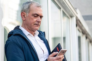 Yetişkin çekici bir adam cep telefonu kullanıyor ve dizüstü bilgisayarını sokakta tutuyor.