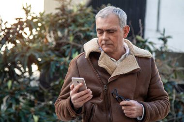 Sokakta cep telefonu kullanan ceketli olgun bir adam.