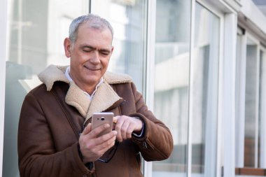 Sokakta cep telefonu kullanan ceketli olgun bir adam.