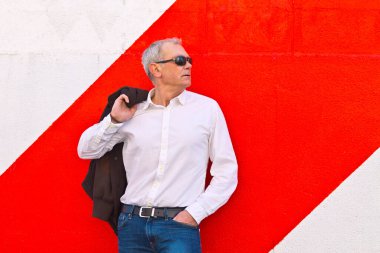 Duvara yaslanmış güneş gözlüklü zarif olgun bir adam.