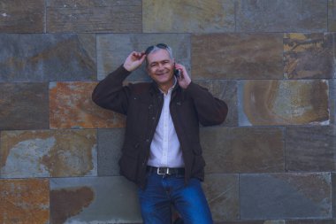 Güneş gözlüklü gülümseyen adam duvar arkası cep telefonu kullanıyor.