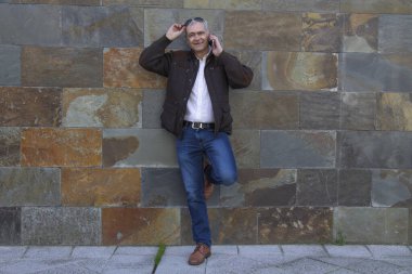 Güneş gözlüklü gülümseyen adam duvar arkası cep telefonu kullanıyor.