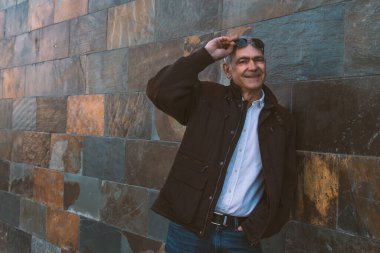 Duvarda kot pantolon ve ceket giyen yetişkin bir adam.