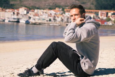 Gülümseyen genç adam rahatlamış ve sahilde eğleniyor.