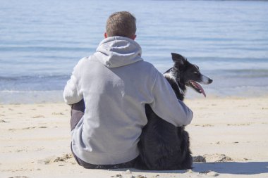 Plajda köpekle rahatlamış genç adamın portresi.