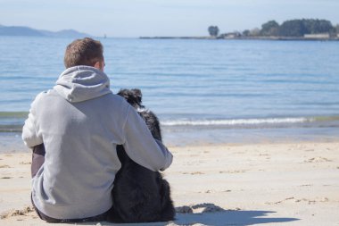 Plajda köpekle rahatlamış genç adamın portresi.