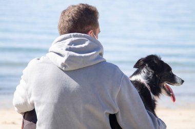 Plajda köpeğiyle maske takan genç bir adam.