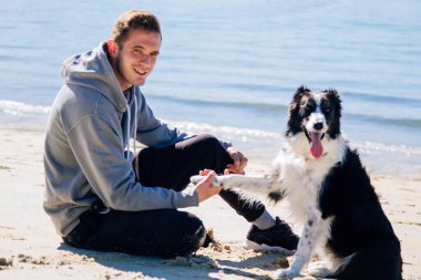 Plajda köpeğiyle genç bir adamın portresi.