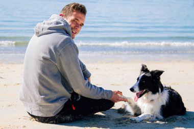 Plajda köpekle rahatlamış genç adamın portresi.