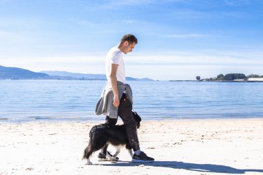 Rahat genç adam sahilde köpekle oynuyor.