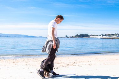 Rahat genç adam sahilde köpekle oynuyor.