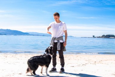 Genç adam sahilde köpeğiyle oynuyor.