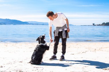 Genç adam sahilde köpeğiyle oynuyor.