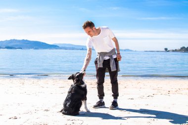 Genç adam sahilde köpeğiyle oynuyor.