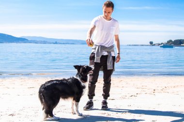 Genç adam sahilde köpeğiyle oynuyor.