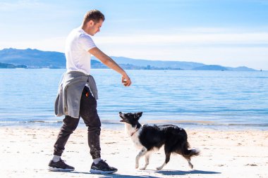 Genç adam sahilde köpeğiyle oynuyor.