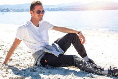 Gülümseyen genç adam rahatlamış ve sahilde eğleniyor.