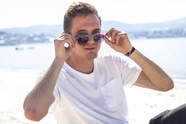 Gülümseyen genç adam rahatlamış ve sahilde eğleniyor.