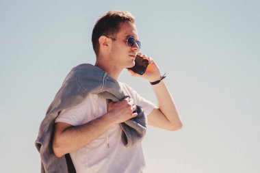 Genç adam sahilde yürüyor ve cep telefonuyla konuşuyor.