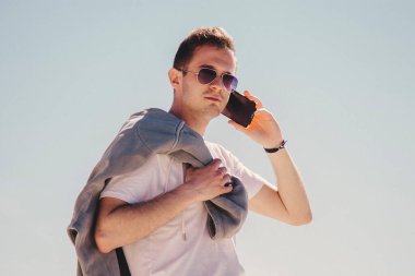 Genç adam sahilde yürüyor ve cep telefonuyla konuşuyor.