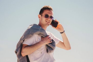 Genç adam sahilde yürüyor ve cep telefonuyla konuşuyor.