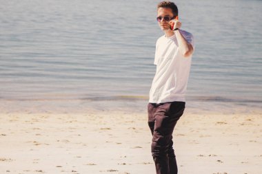 Genç adam sahilde yürüyor ve cep telefonuyla konuşuyor.