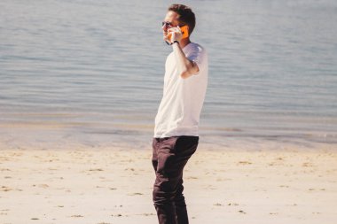 Genç adam sahilde yürüyor ve cep telefonuyla konuşuyor.
